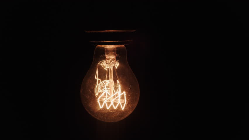 Incandescent light lamp bulb flickering on black background in dark room close-up