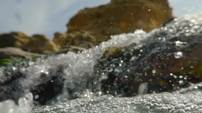 Split level underwater shot of camera descending underwater into fast flowing mountain stream, lots of air bubbles moving under surface, macro video, super slow motion