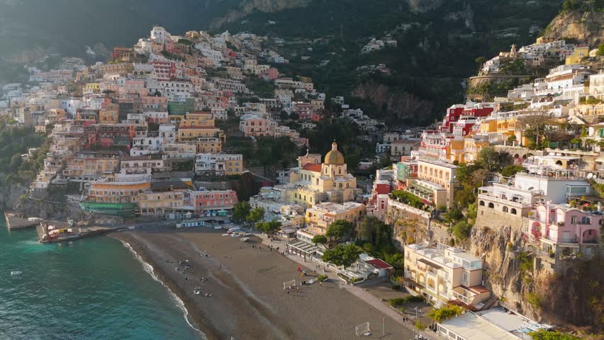 Famous tourist resort of the Amalfi coast - Positano at sunset. Flying above colorful houses, church and beach with turquoise water - Positano village, Italy. UHD, 4K