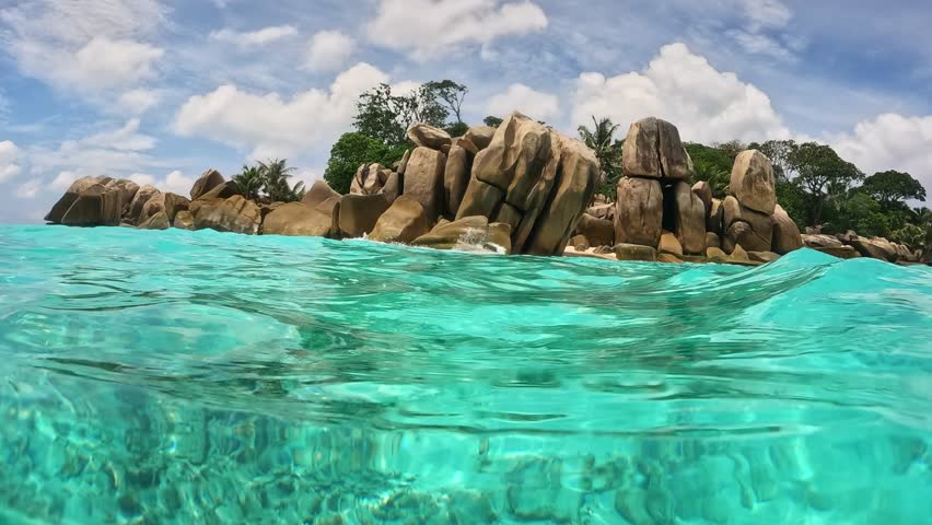 Stunning underwater view of crystal clear water and rocky shoreline in tropical paradise. Half underwater slow motion of turquoise water, rocks and trees on tropical island in Seychelles 