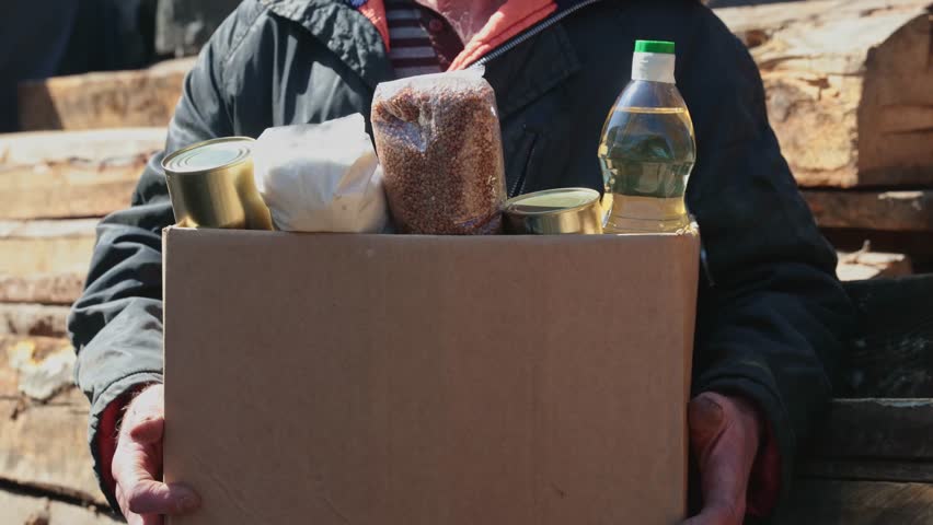 Concept humanitarian aid community charity donations center with sunlight. Homeless refugee is holding box food