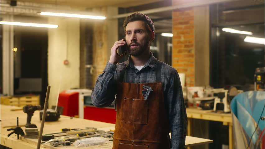 Professional Caucasian carpenter guy speaking call mobile phone in workshop artist worker wood master communicate architect male using telephone connection network man builder contact client carpentry