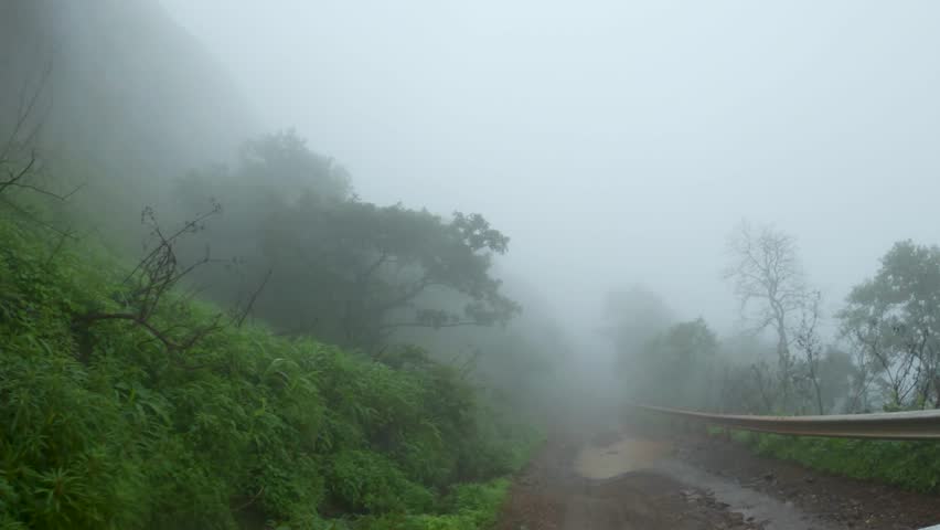 4K POV shot of a vehicle moving on a muddy road covered by fog in the middle of the forest in Sahyadri hills during the monsoon season at Maharashtra, India. Vehicle driving during foggy weather.