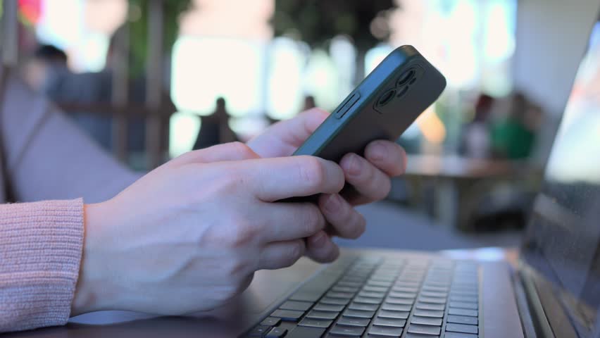 A person uses a smartphone while working on a laptop in a vibrant caf setting