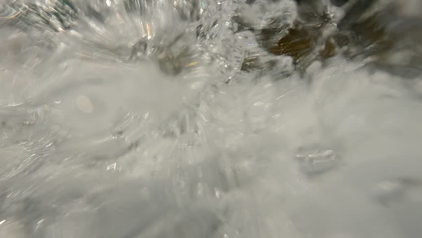Waterfall water flow falling down splashing water droplets into camera lens sparkling in bright sunlight, super slow motion, extreme close-up