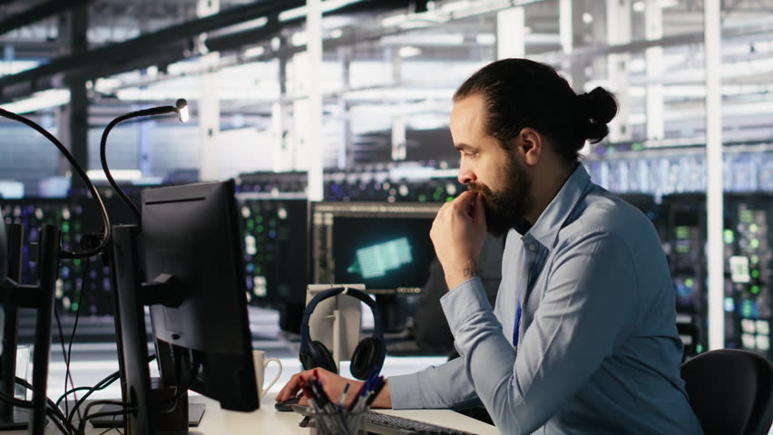Panicked engineers in data center react to ransomware warning on PC display, scrambling to launch emergency response protocol. IT staff urgently trying to fix hacked infrastructure systems, camera A