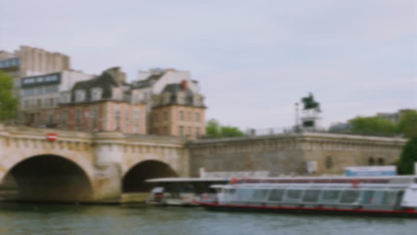 View of the arch bridge stone Pont Neuf, the Equestrian Statue of Henri IV, the Seine River, the embankment of the Island Cite. The Vedettes du Pont Neuf tour boat. Out of focus. Paris, France.