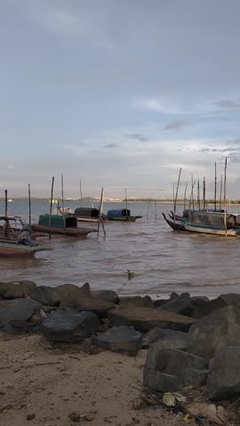 Fishing boats anchored by the shore at sunset near a calm coastal village