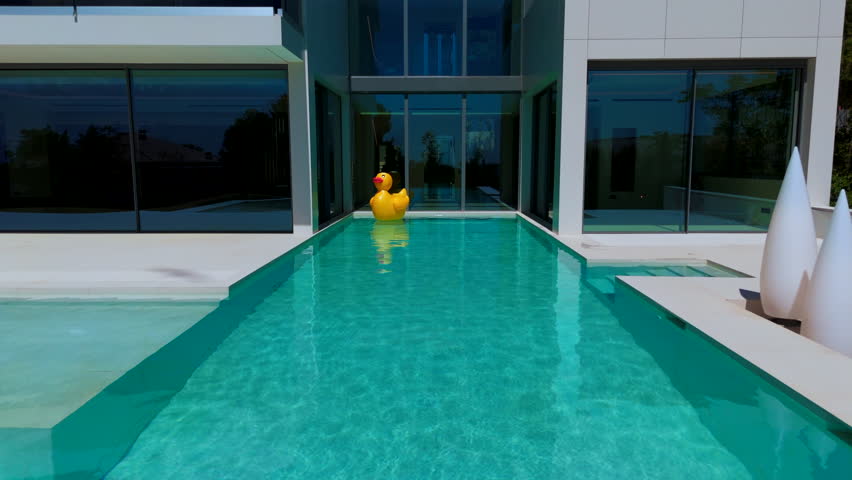 swimming pool with blue water. There is a yellow duck toy floating on the surface. Small waves are seen around the toy. The atmosphere looks calm and refreshing. High quality 4k footage