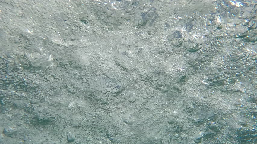 Close-up of below water surface on heavy rainstorm, raindrops falling on the water, bottom-up view. Underwater view of power rainfall. Heavy waterdrops of rainstorm below water