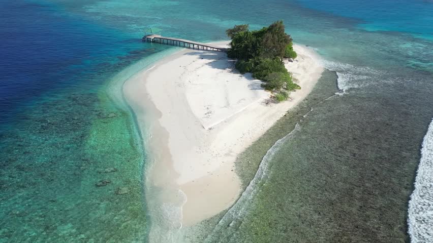 Aerial view of desert island in blue sea. Lonely building and pier at the coastline. Maldives
