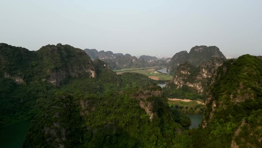 Drone shot showcasing Vietnam’s iconic limestone karst landscape with a serpentine river carving through the jungle-clad cliffs and rural rice fields in early daylight.