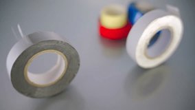 Two insulating tape rolls, gray and white, roll on a reflective glass table, with blurred colorful tapes in the background. - Powered by Shutterstock - Get 15% off with code: PIKWIZARD15