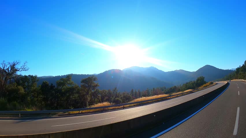 Sunlight streaming over winding mountain road, revealing scenic driving experience with expansive landscape and golden morning rays illuminating empty asphalt path through wilderness
