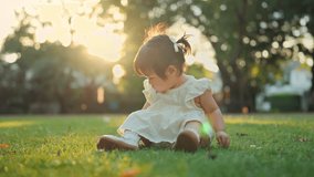 Happy little asian baby girl sitting on green grass lawn, touching and exploring nature in backyard garden during summer, sunlight sunset – learning, growth and outdoor fun - Powered by Shutterstock - Get 15% off with code: PIKWIZARD15