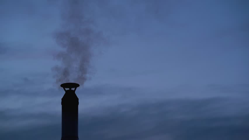 Black smoke comes out of a chimney against a dark blue sky