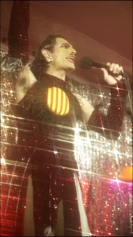 A talented drag queen takes the stage, delivering an energetic musical performance singing and dancing in queer LGBTQ venue.