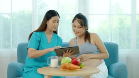 Female nutritionist uses a tablet to introduce foods and fruits with vegetable, to young pregnant Asian woman with a potbelly. The pregnant woman consults a medical nurse about improving her diet - Powered by Shutterstock - Get 15% off with code: PIKWIZARD15