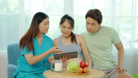 Female nutritionist uses a tablet while consulting about essential healthy foods to Asian family, Pregnant mother and husband listening to advice from medical nurse to future parenthood.	 - Powered by Shutterstock - Get 15% off with code: PIKWIZARD15