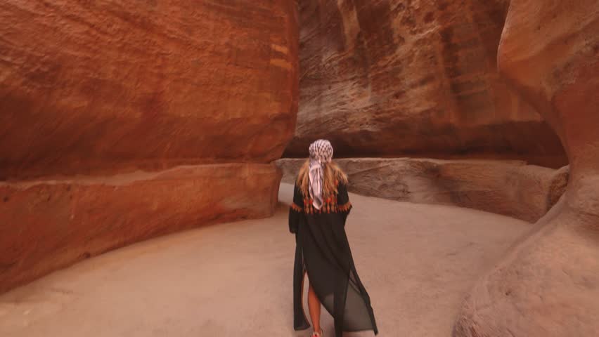 Woman walks through the narrow sandstone canyon known as the Siq, the main entrance to the ancient city of Petra, Jordan.