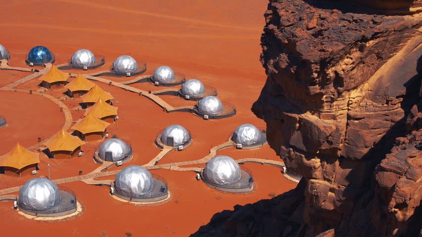 Elevated view of a futuristic human colony base on a red planet surface next to rocky cliffs. Mars base concept with domes and tents.