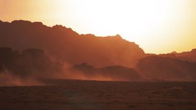 Desert landscape with rock formations silhouetted against the sky at sunrise or sunset with dust blowing across the ground in Wadi Rum, Jordan. - Powered by Shutterstock - Get 15% off with code: PIKWIZARD15