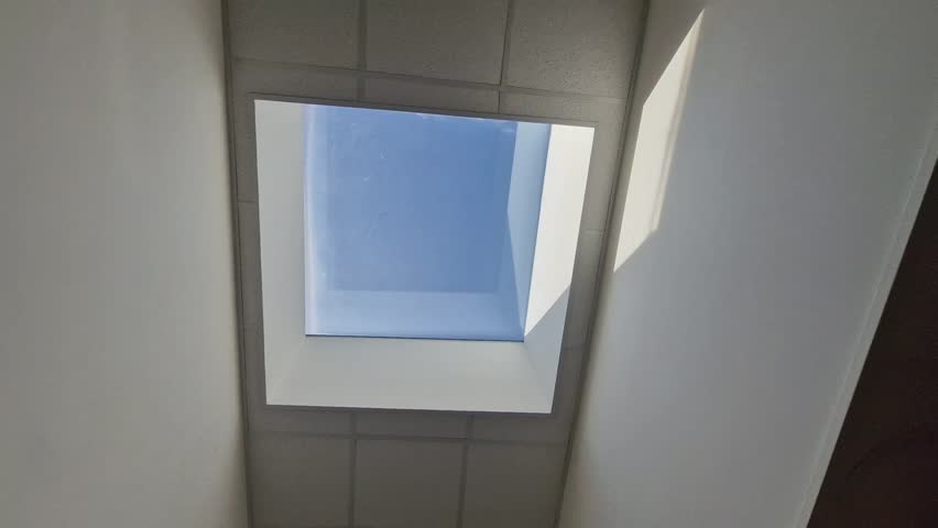 high above the head is a rectangular window illuminating the entire area of the hall with natural light. the window is a rectangular skylight. the walls are pure white plaster