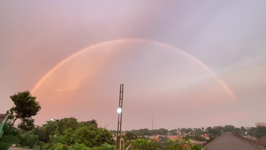 Rainbow in the evening sky after rain, a semicircular rainbow in the distance above the roof of a house