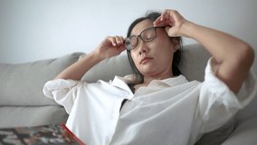 Tired Asian woman in white shirt rubs her eyes while resting on couch after screen time. A realistic and emotional moment of fatigue and digital burnout in modern lifestyle. - Powered by Shutterstock - Get 15% off with code: PIKWIZARD15
