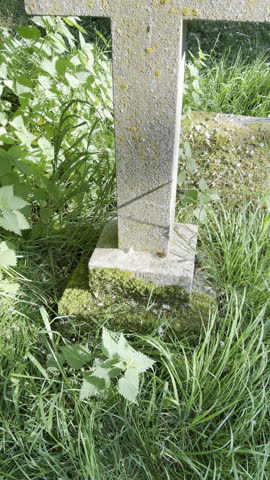 Vertical video - Closeup slow tilt shot of an old stone cross in a cemetery graveyard, bearing the simple inscription, R.I.P.