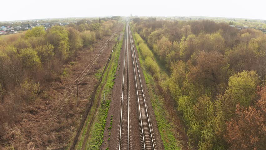 Railway track stretching through verdant spring countryside, showcasing expansive rural landscape with serene green scenery and distant horizon