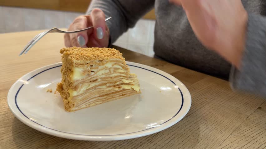A 54 year old woman enjoys and eating a slice of Napoleon cake in restaurant. Sweet dessert
