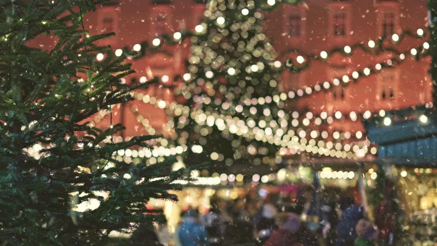 People stroll through the market square with decorated tree at Christmas market. Holiday market ambiance fills the air with festive lights and cheerful gatherings, first snow falling