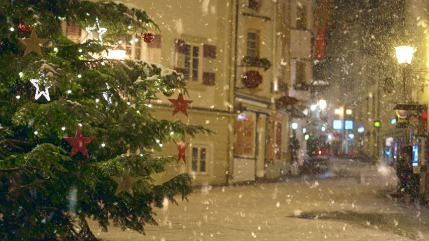 Snow falls in the city during the Christmas and New Year holidays. Snow falls over decorated streets in charming town square during holiday season. Winter in the city