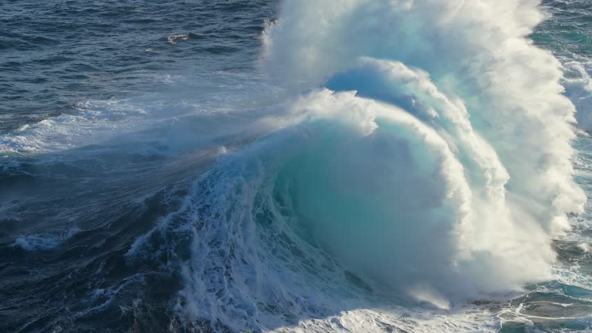Massive ocean waves crash against rocky shore, creating impressive splashes and mist near coastal cliffs. Aerial slow motion shot of big epic waves surf crash