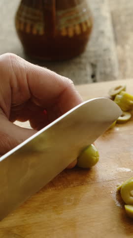 Vertical video. Slicing vegetables. Cooking process. Female hands are cutting olives on chopping board. 