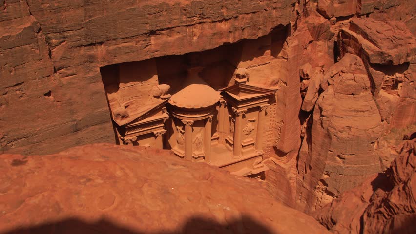 High angle view looking down at the ancient Treasury building facade carved into the sandstone rock walls in Petra, Jordan.