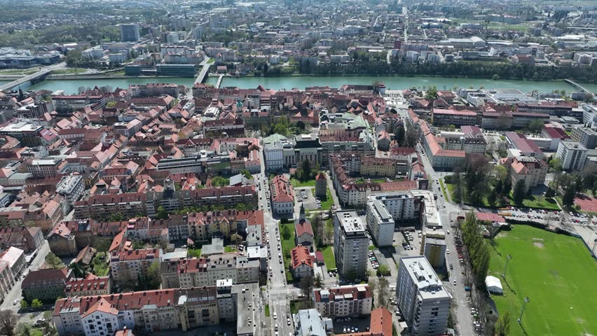Aerial footage of Maribor, Slovenia on bright spring day. Rooftops, city streets, historic buildings are surrounded by blooming trees and green spaces, offering perfect blend of culture and nature