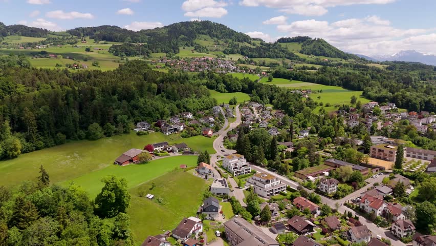 Drone flight over swiss city of Hinwill with luxury apartment houses in idyllic mountains of Switzerland. Aerial forward wide shot. Green forest landscape and hills in distance. Modern buildings.