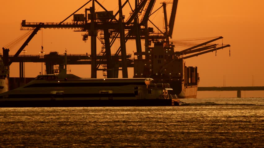 Container ship docking at sunset in a busy harbor