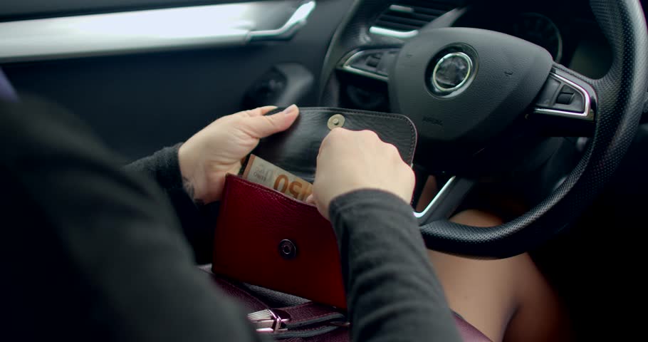 A woman is seated in her car, carefully opening her wallet to take out some cash for her upcoming transaction needs