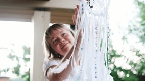 Portrait of a cute young woman in a white dress with a dreamcatcher. The craftswoman made the dreamcatcher herself with white feathers and ribbons. The dreamcatcher sways in the wind. The woman smiles - Powered by Shutterstock - Get 15% off with code: PIKWIZARD15