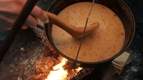 Mouth-watering vegetable soup with mushrooms and cheese is being stirred with wooden spoon in camp pot while cooking over an open fire during hiking trip. High angle - Powered by Shutterstock - Get 15% off with code: PIKWIZARD15