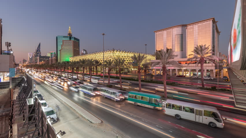 Aerial day to night timelapse of King Fahd Road in Riyadh, Saudi Arabia. Bustling traffic panorama with cars and taxis near the illuminated National Library surrounded by modern towers and skyscrapers