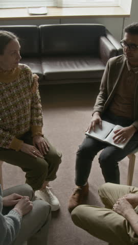 Vertical overhead view of diverse support group and their therapist with notebook sitting in circle, holding hands and creating safe space for emotional sharing and collective healing