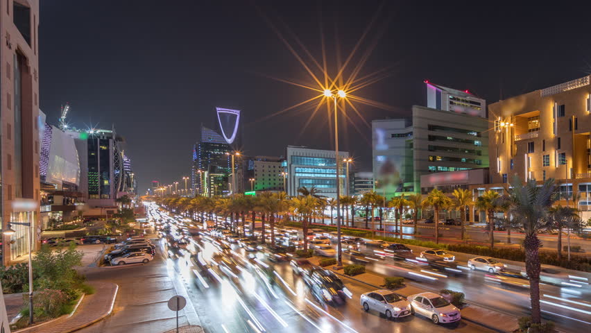 Cityscape aerial night timelapse of Riyadh, Saudi Arabia, featuring illuminated famous towers, skyscrapers, King Fahd Road and busy traffic. Palms and streetlights line the main highway through a city