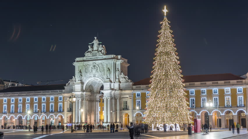 Commerce Square in Lisbon illuminated at Christmas hyperlapse, with a towering tree and arch at night. Timelapse of the festive atmosphere featuring decorations and historic architecture