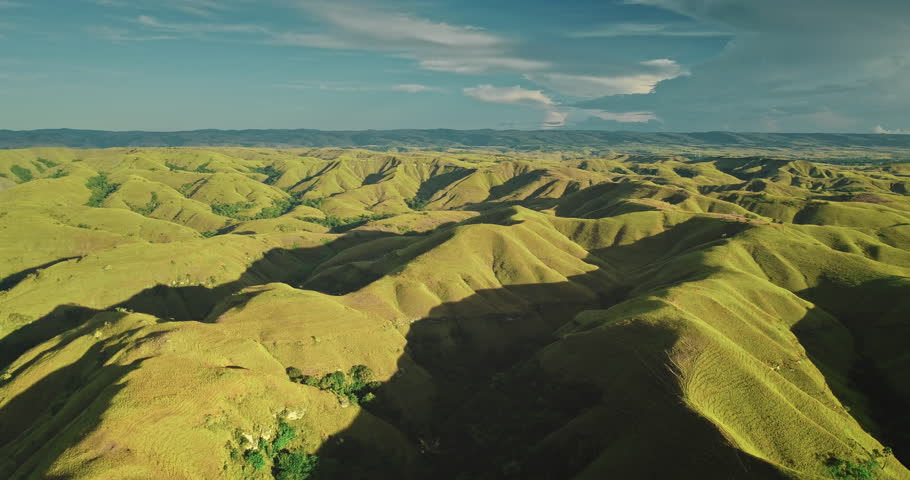 Lush green hills stretch as far as the eye can see, creating a breathtaking landscape under a vibrant blue sky with fluffy white clouds in Sumba Island, Indonesia