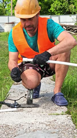 a man in an orange construction vest and helmet solders polypropylene pipes for supply