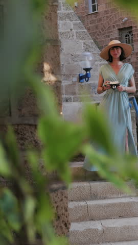 Vertical shot. A female photographer with a camera takes pictures in the city. A young female photographer points the lens and enjoys the process of shooting. travel and content creation.